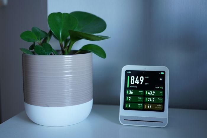 Desktop air quality monitor next to a potted plant showing CO2 and PM2.5 readings